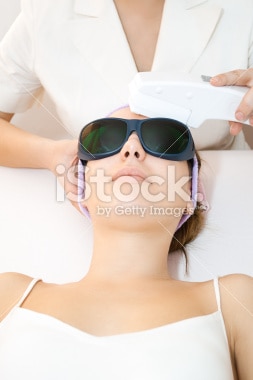 Woman receiving laser facial treatment with protective goggles.